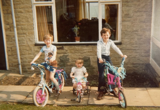 Three children on bikes in front of a house